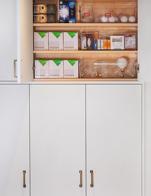 A small closets with three horizontal shelves filled with lightbulbs and vertical cabinets at the bottom